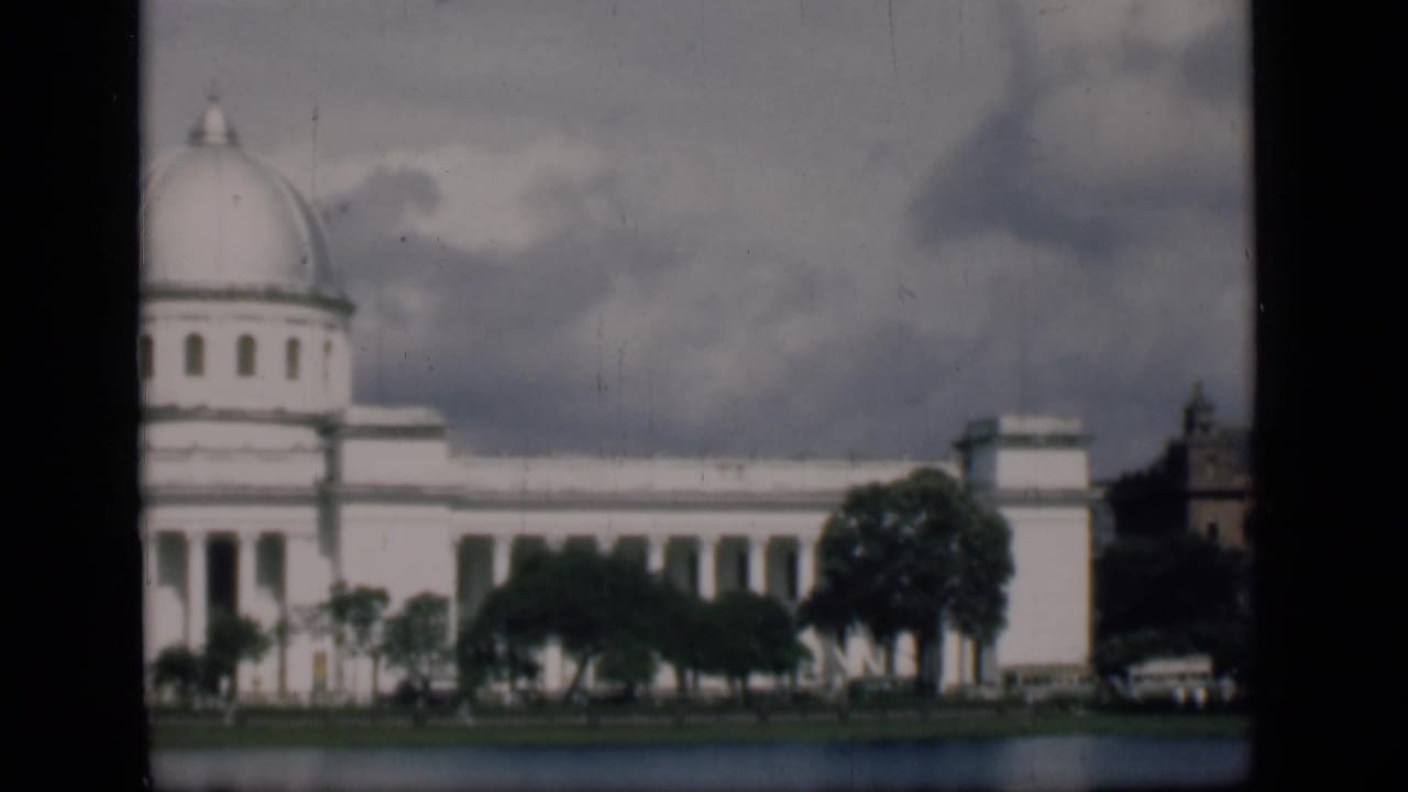 Domed white building, trees, road edge, and small automobile at right.