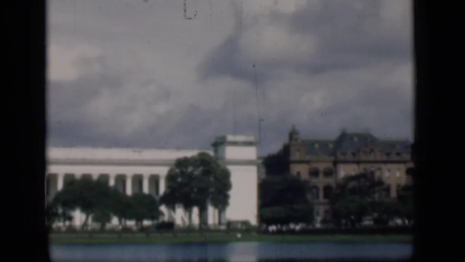 1946 Bombay waterfront architecture with a white classical facade, neighboring brown building, trees, and overcast sky.