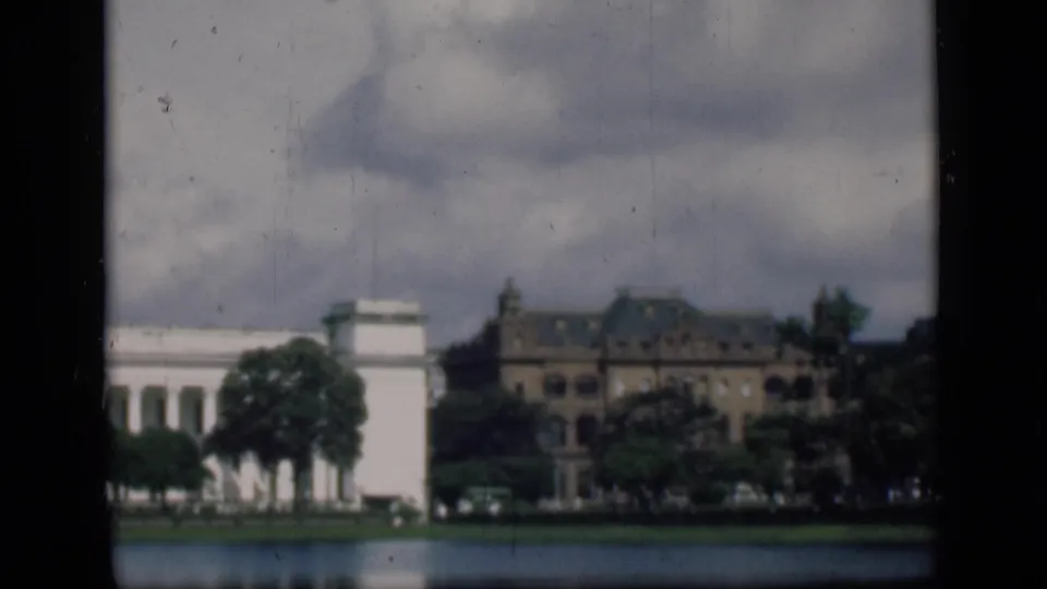 1946 Bombay scene across the water with white and brown buildings, trees, heavy clouds, and visible 8mm film borders.