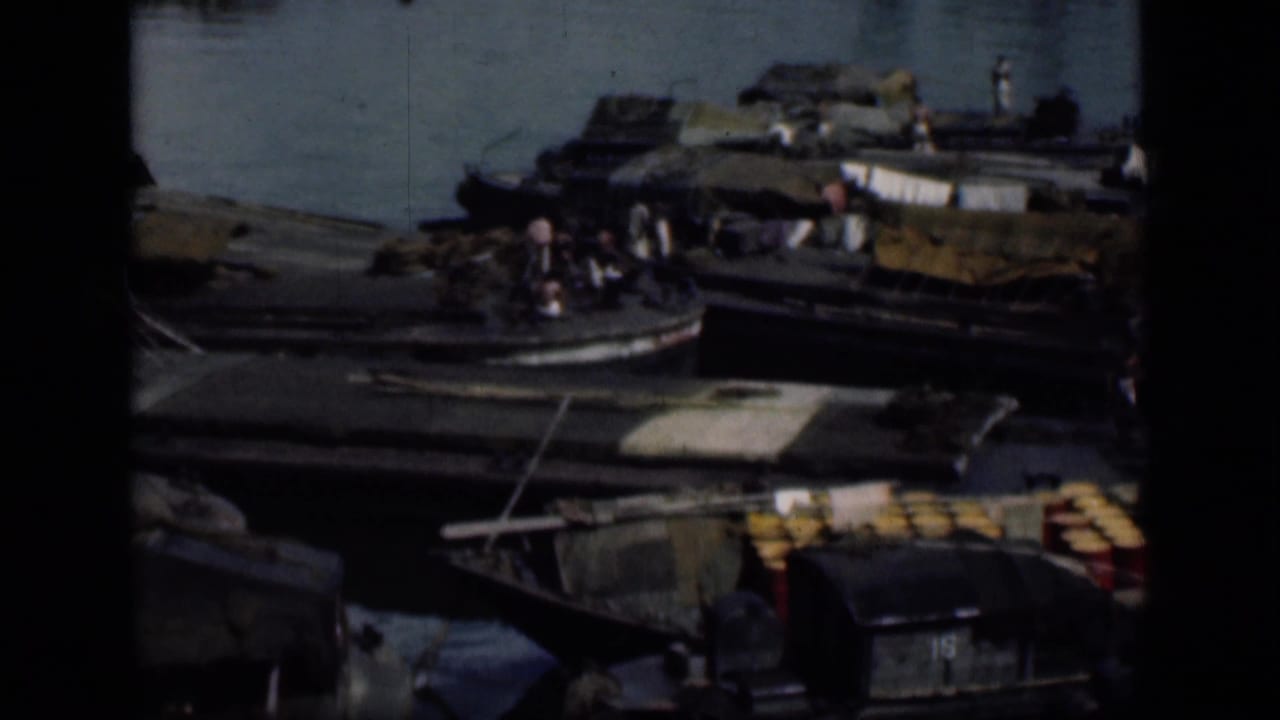 Wooden boats crowded along a waterfront with people and covered cargo visible.