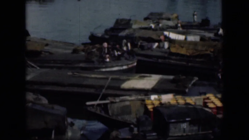 1946 Bombay waterfront view with moored wooden boats, people on deck, covered cargo, barrels, and water beyond.