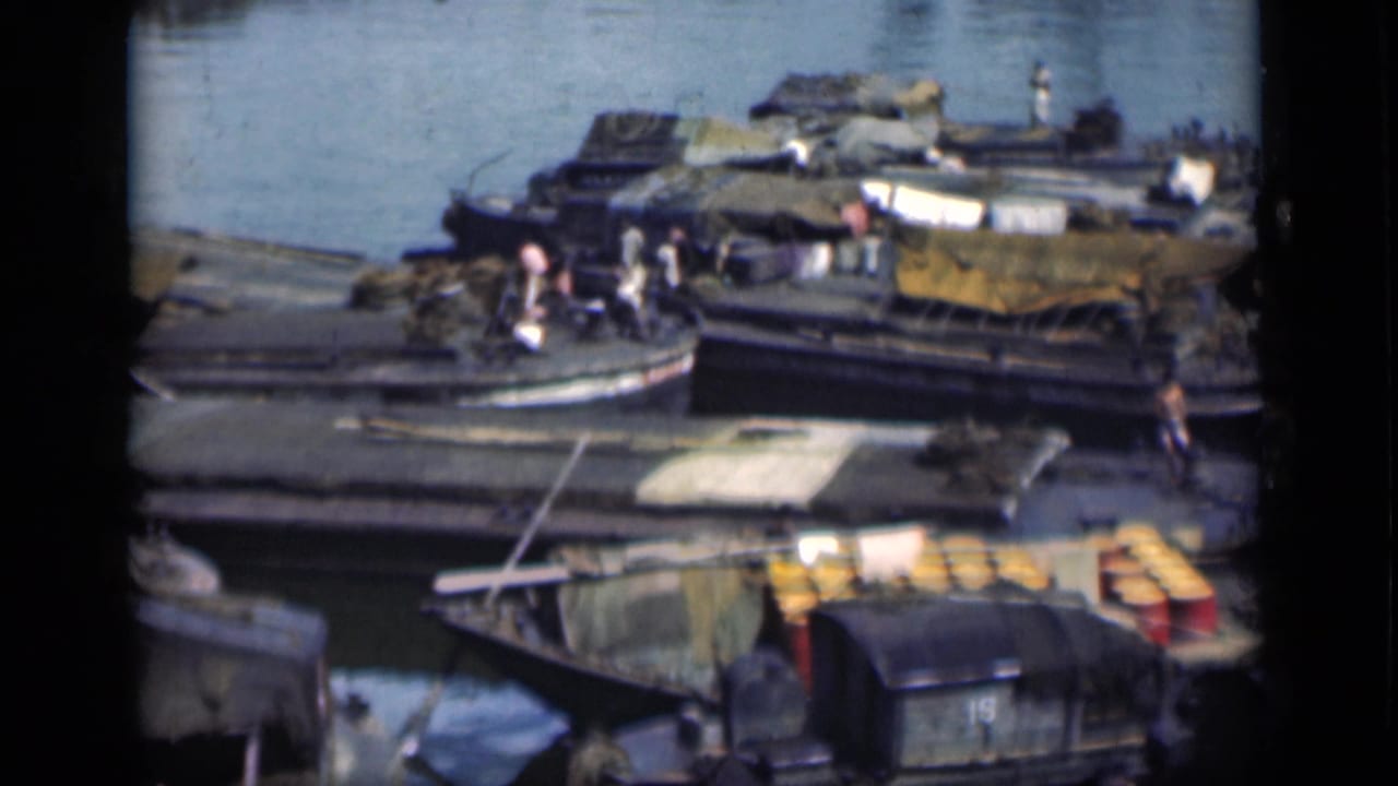 Moored wooden vessels, cargo covers, and people beside the water.