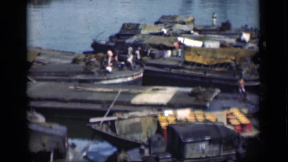 1946 Bombay harbor scene showing wooden boats packed near shore, with people, tarps, barrels, and pale water in the background.