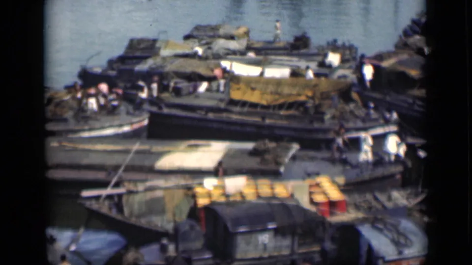 1946 Bombay waterfront view with moored wooden boats, covered cargo, tarps, dock edges, and small figures moving among the vessels.
