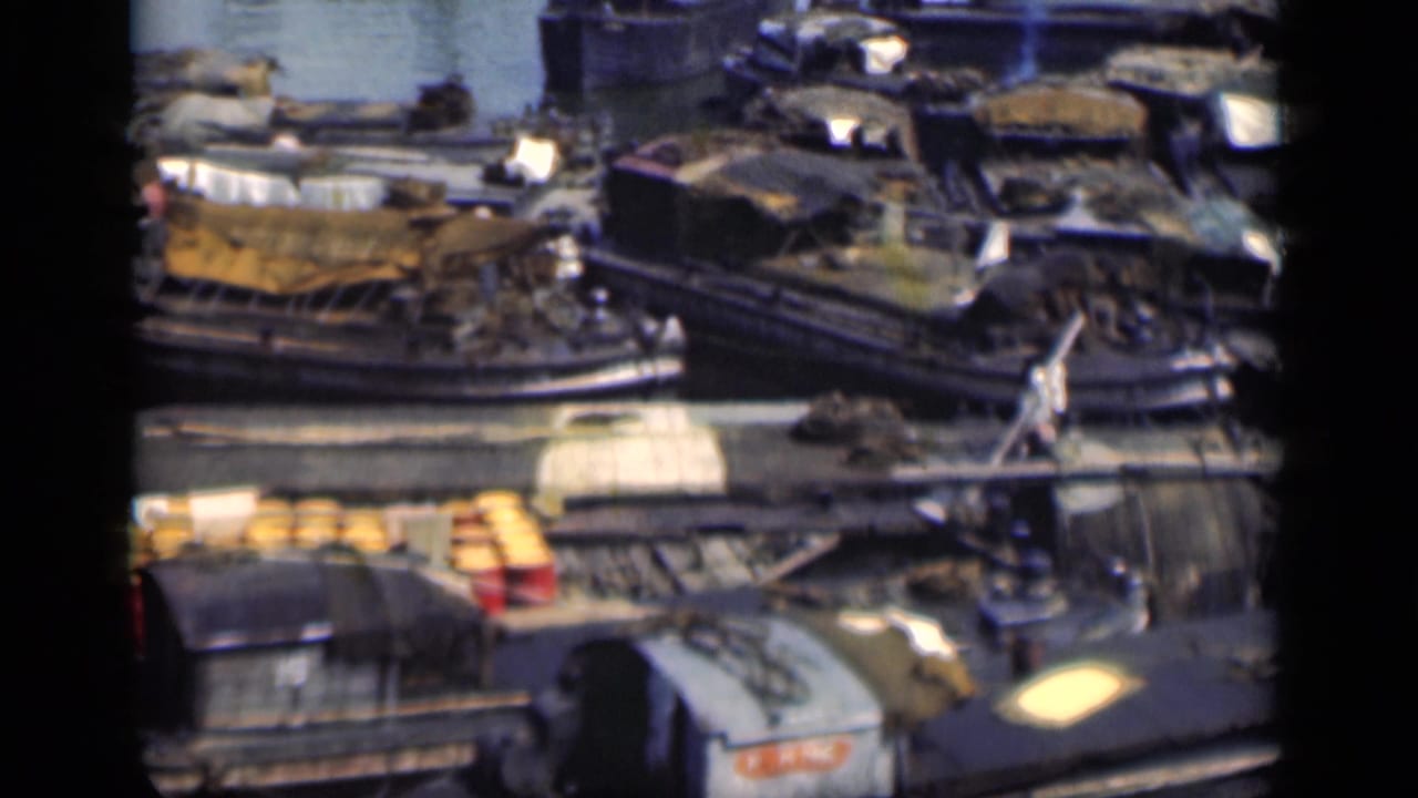 Cluster of moored boats with tarps, cargo, and people standing near the dock.