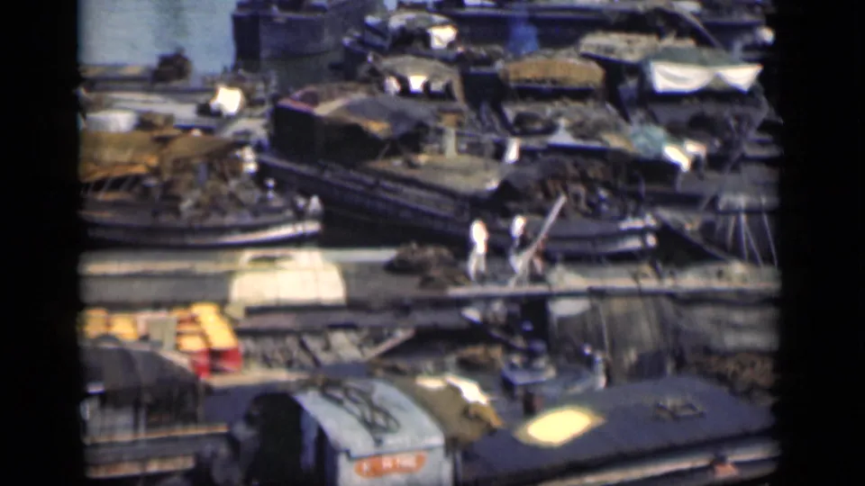 1946 Bombay shipyard or dock view with layered wooden boats, covered barges, cargo stacks, and people crossing between vessels.