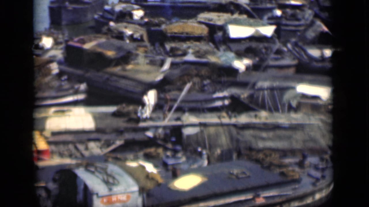 Crowded waterfront with boats, planked walkways, scattered gear, and small figures near the lower left.