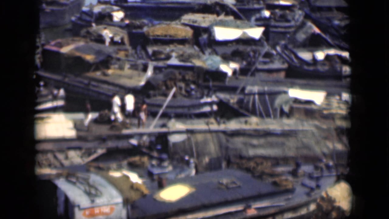 Elevated view of cluttered boats, a narrow walkway, and people crossing near harbor equipment.