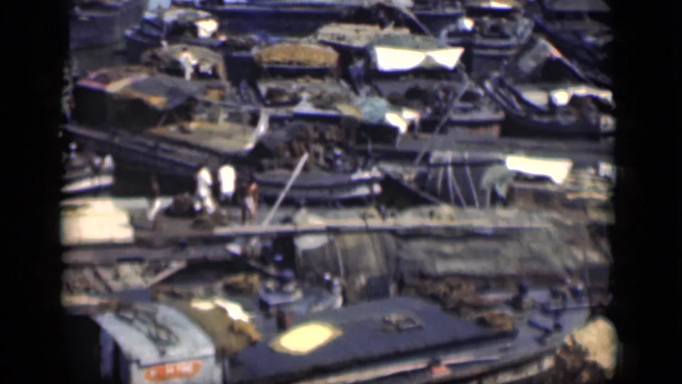 Bombay harbor area in 1946 with tightly packed boats, a narrow crossing, pedestrians, and work gear visible in soft 8mm color.