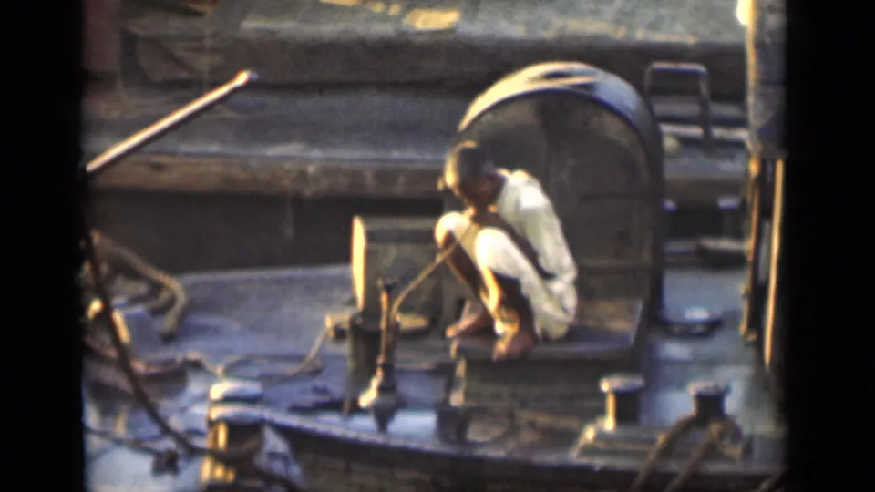 In 1946 Bombay footage, a crouched man works with a hose or line on a boat deck surrounded by ropes and fittings.