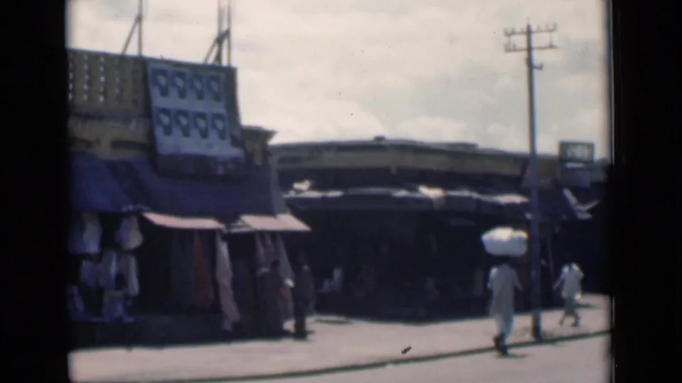 Calcutta street scene from 1946 with shaded shopfronts, a visible sign and pedestrians crossing the frame.