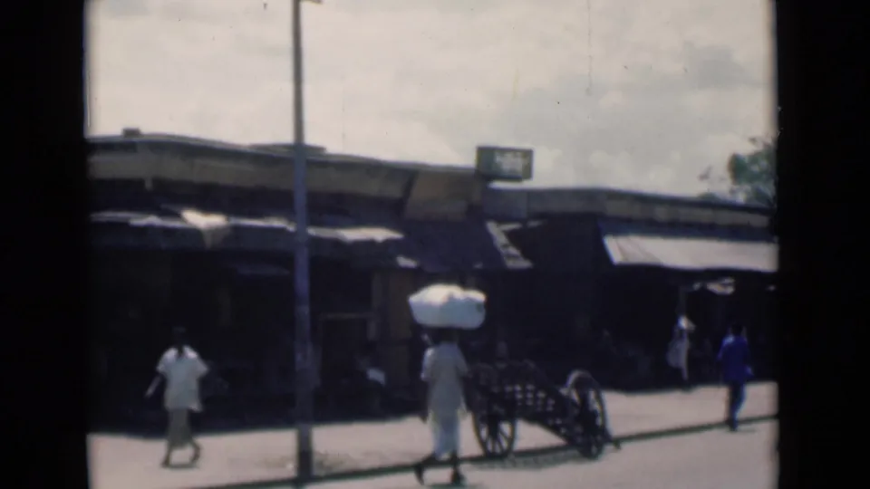 Late frame of the 1946 Calcutta street scene with pedestrians, a handcart, shop awnings and a telephone pole.