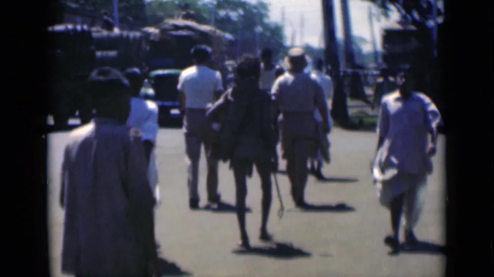 Calcutta, 1946, with pedestrians seen from behind walking past large military-style trucks and tall roadside trees.