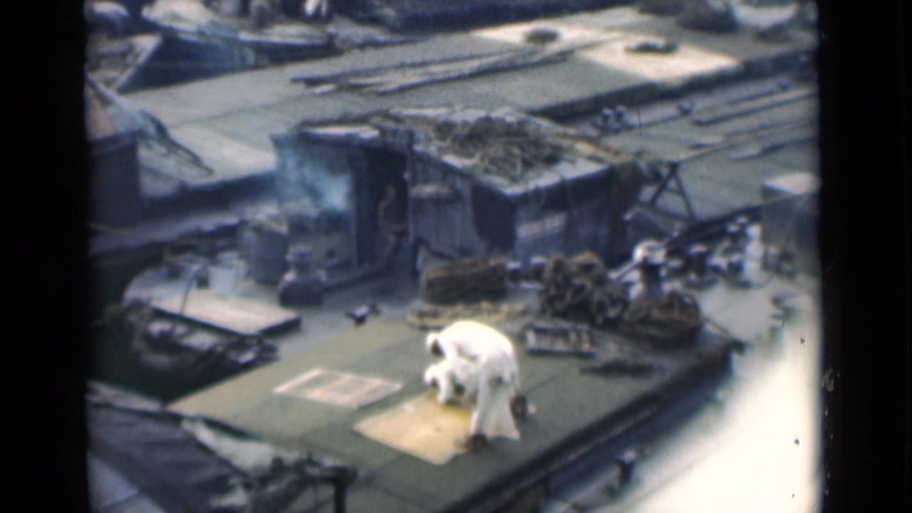 Man in white clothing kneeling on a rooftop near ropes and roof equipment.