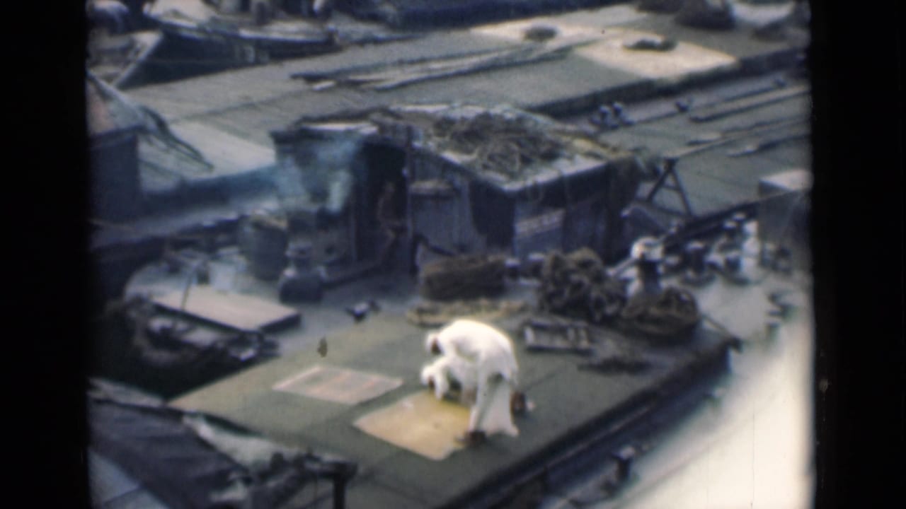 Man in white bends forward on a rooftop beside coiled rope and roof fixtures.