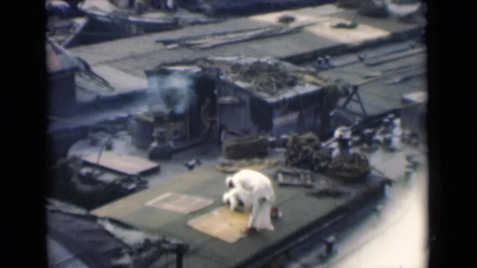 A 1946 Calcutta rooftop ritual continues as the man kneels low near a small mat or marked patch, with ropes and roof hardware around him.