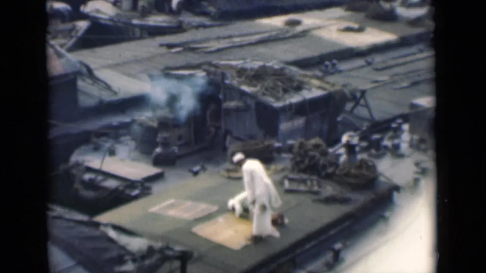 Near the end of the clip, the man in white rises or bends on the rooftop while coiled rope and surrounding roof structures remain visible.
