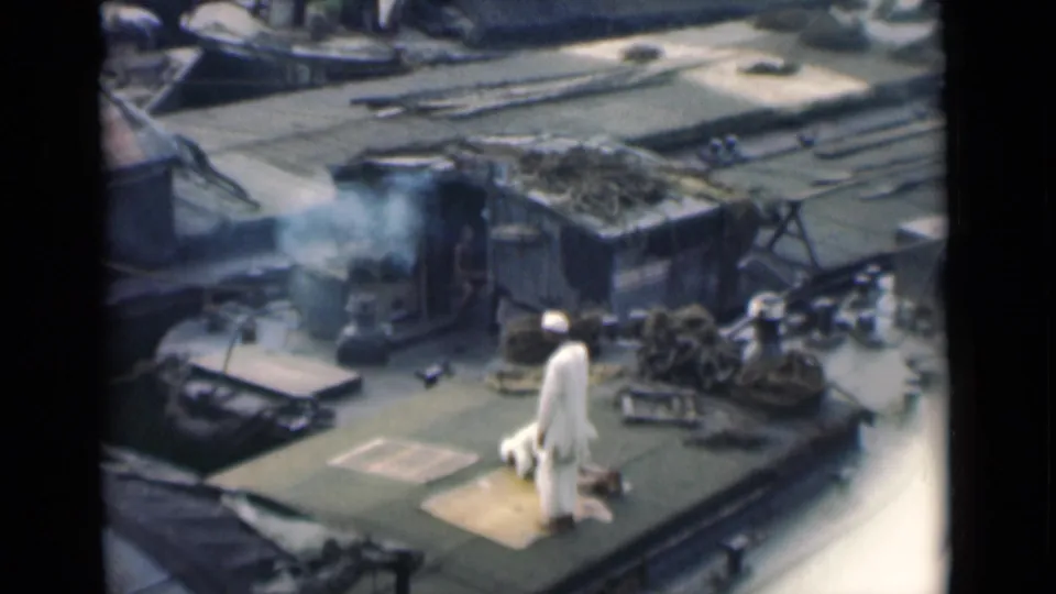 1946 Calcutta shipboard frame showing a man in white near a prayer mat, with ropes, cargo-like materials, and smoke visible on deck.