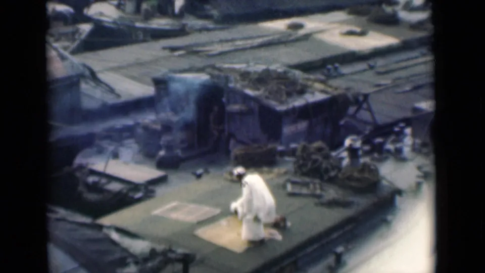 High-angle 8mm frame from 1946 Calcutta showing a man kneeling in prayer on a ship deck near smoke, ropes, and equipment.