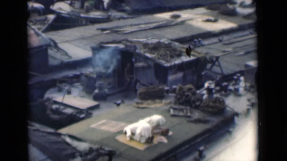 1946 Calcutta ship-deck footage shows a man in white bowing low on a prayer mat amid ropes, deck gear, and smoke.