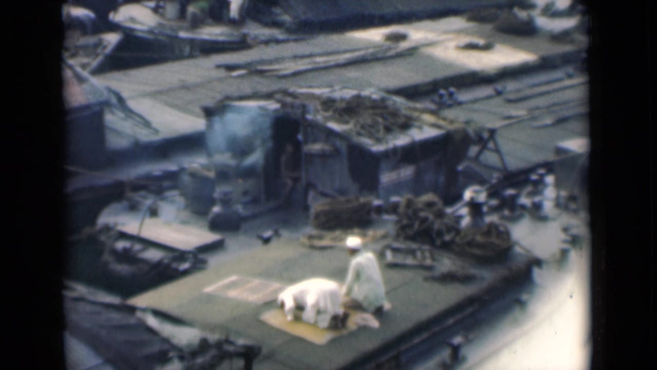 Man prostrating on a rooftop mat as another white-clad figure stands nearby.