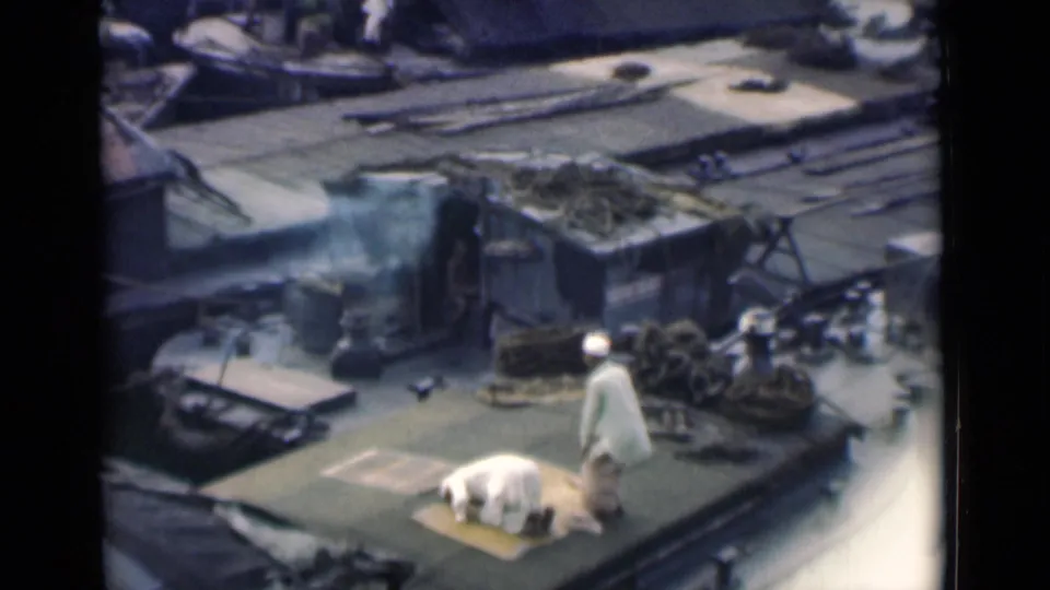 A white-clad figure stands on a damaged Calcutta rooftop as a man continues prostration on a mat nearby.