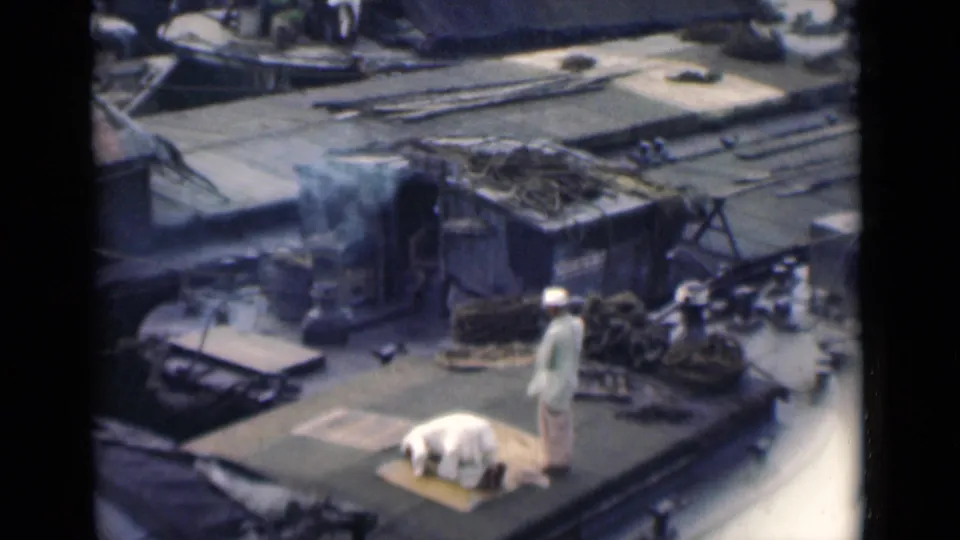 On the Calcutta rooftop, the standing figure remains beside the prayer mat while smoke drifts from the damaged background.