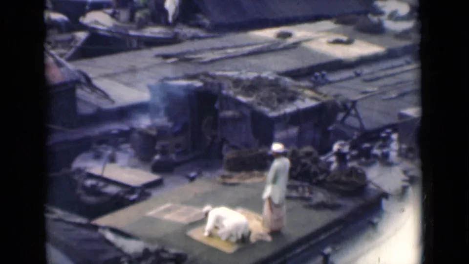A man prostrates on a prayer rug as another stands nearby on a working boat deck in the 1946 Calcutta home movie.