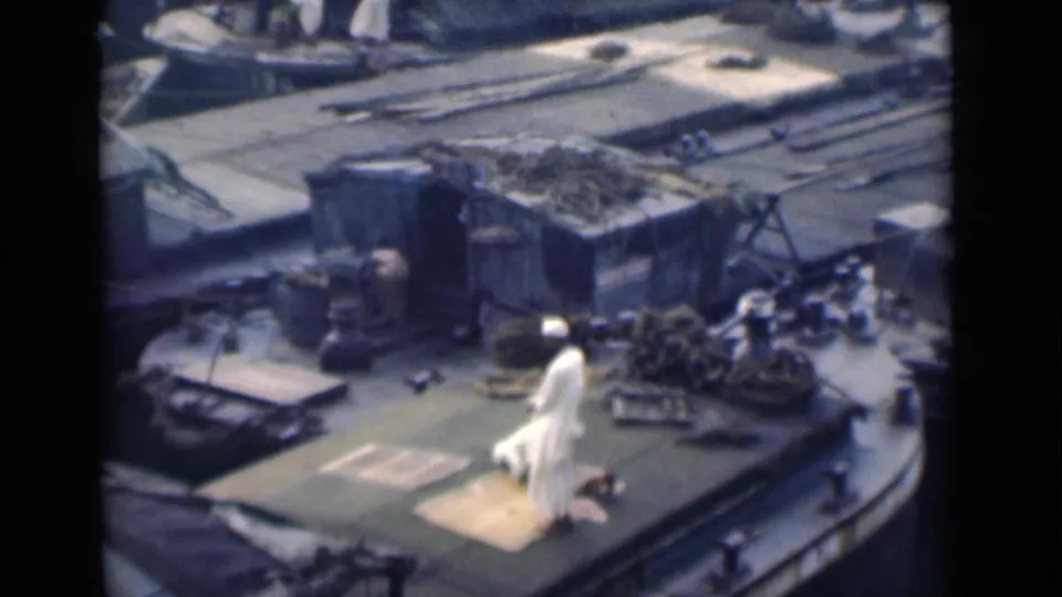 1946 8mm frame from Calcutta, India, showing a Muslim man in white clothing on a prayer rug on a ship deck.