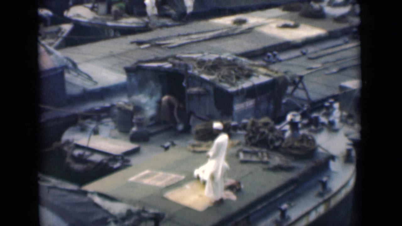 A man in white stands near a mat on a boat deck while another figure is low to the deck nearby.