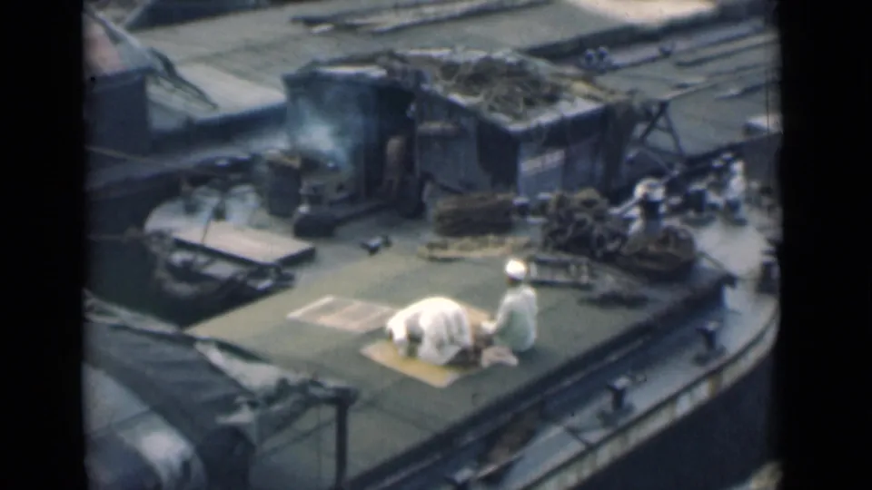 In the closing frame, both men are low to the deck beside the mat, with coiled ropes, railings, and a small cabin visible around them.