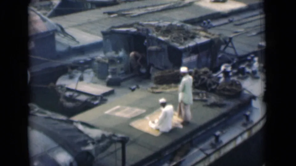 The final frame shows one man seated on the prayer mat and another standing nearby on a cluttered boat deck in 1946 Calcutta footage.