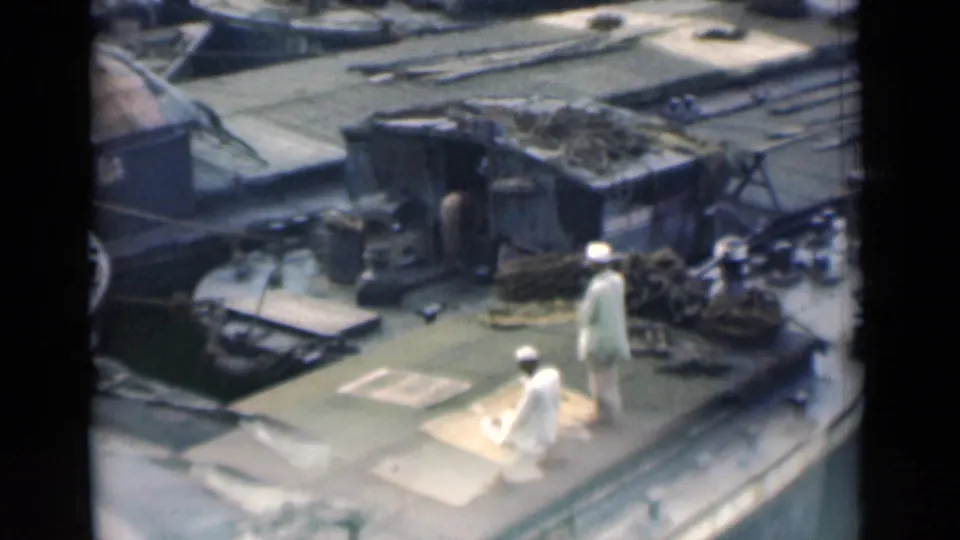 1946 Calcutta 8mm frame showing two men in white traditional clothing on a working boat deck, with one kneeling on a mat near bundled gear.