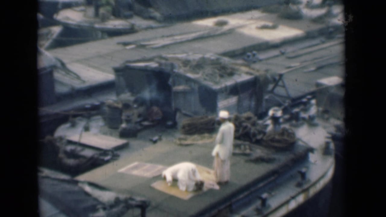 A man bows in prayer on a mat as another man stands nearby on a Calcutta boat deck, with coiled ropes and deck equipment visible.