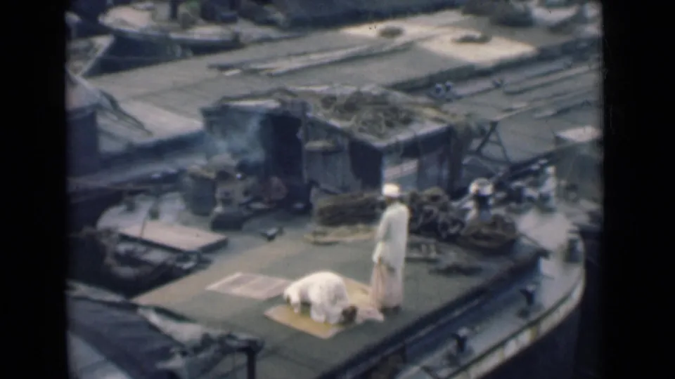 A man remains bowed on a prayer mat while another stands nearby on the 1946 Calcutta boat deck, surrounded by ropes and cargo gear.