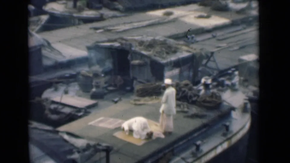 In 1946 Calcutta footage, two men in white garments pray on a small rug on a working boat deck with ropes and cargo nearby.