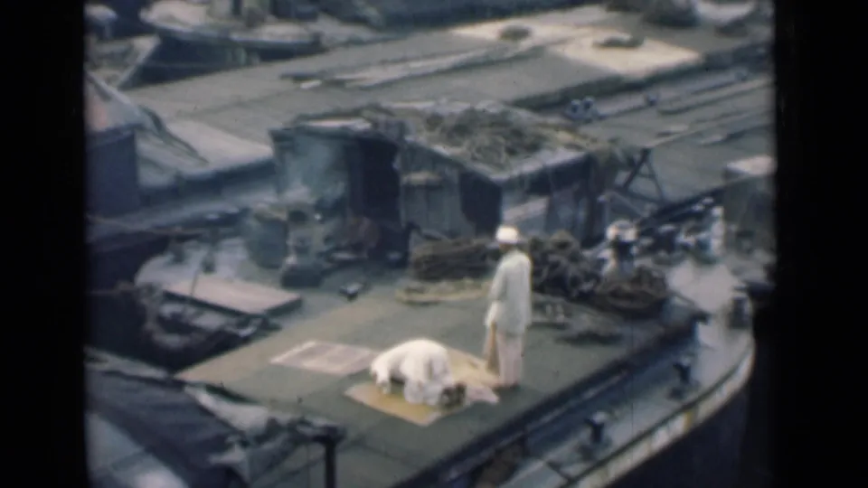 A man prostrates on a rug during prayer on a Calcutta boat deck while another white-clad man stands close by.