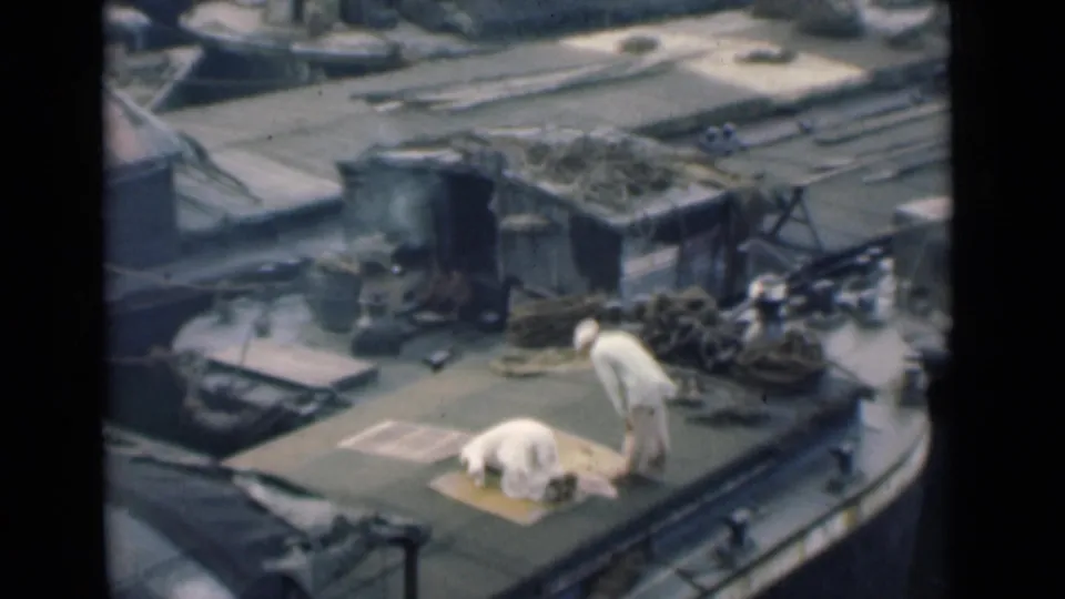 In 1946 Calcutta footage, two men are on a working boat deck as one kneels on a mat and another stands beside ropes and low deck structures.