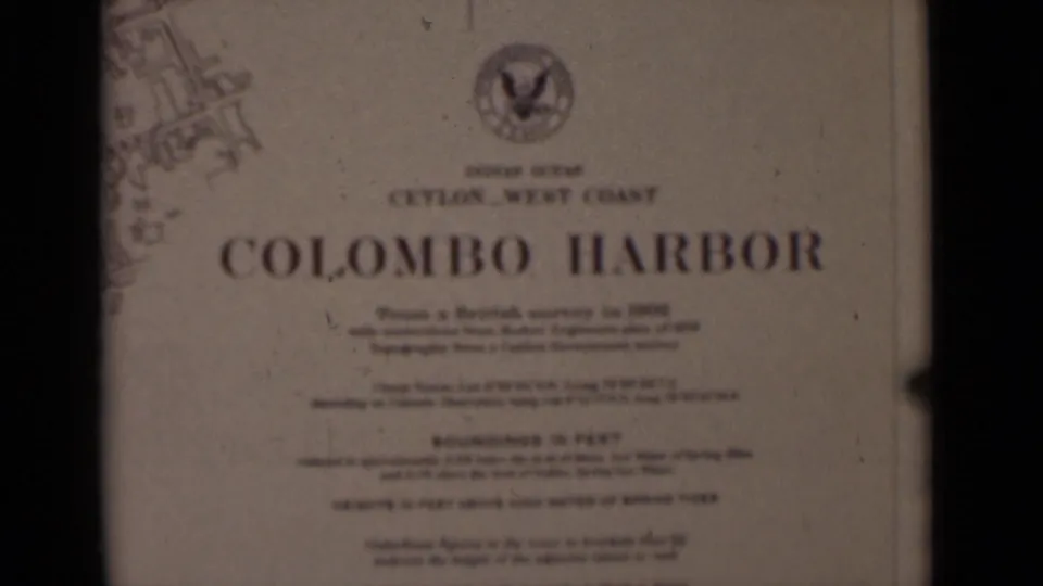 Soft-focus 8mm frame of the Colombo Harbor chart title card, including Ceylon West Coast wording, emblem, and faint chart lines.