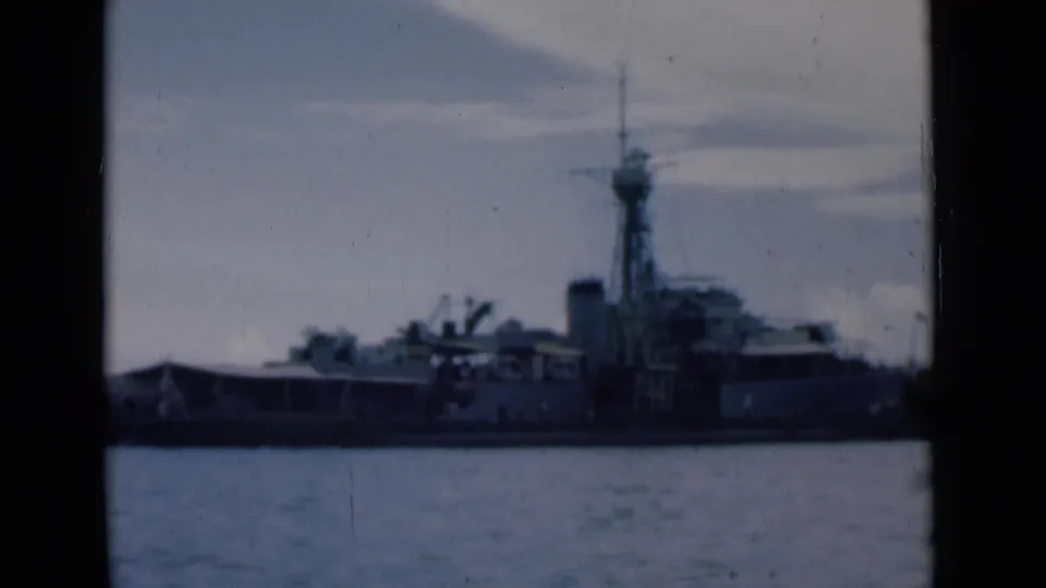 1946 Colombo harbor view of a large grey naval vessel seen broadside across the water on faded 8mm film.