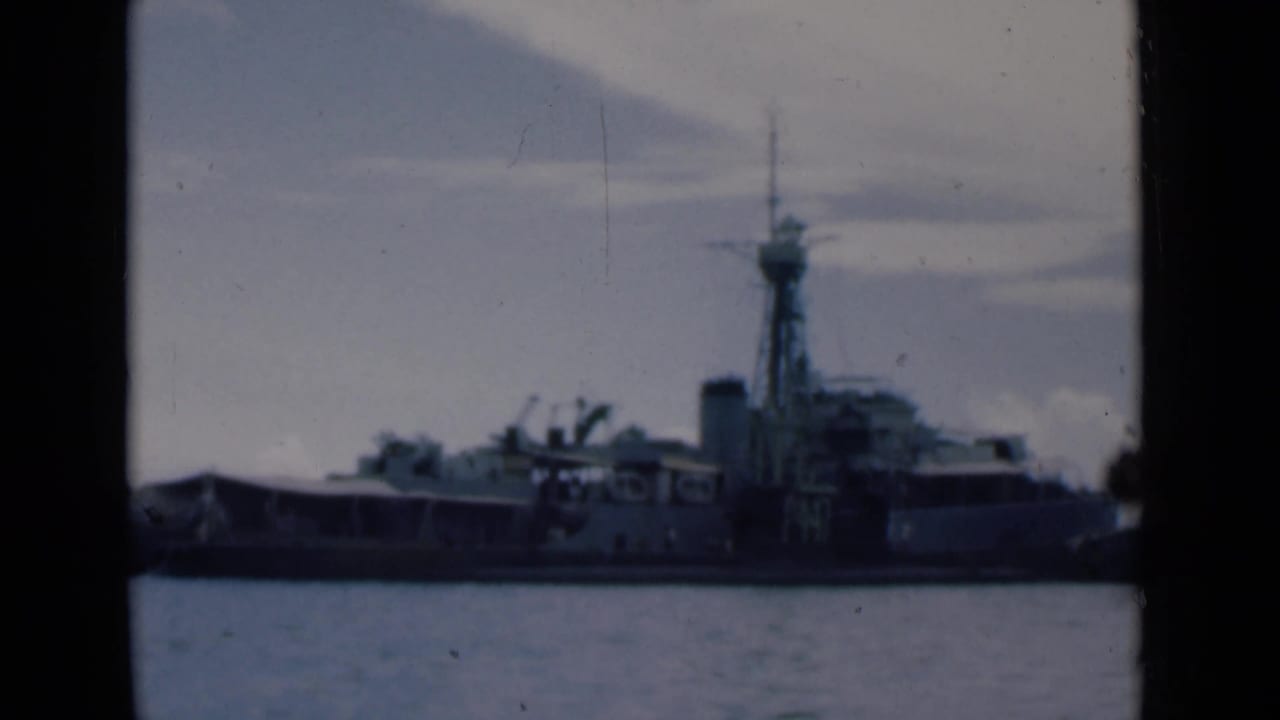 Naval vessel moored near a harbor structure, viewed across water through film-frame edges.