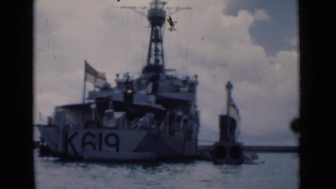 Naval vessel marked K619 moored in harbor beside a small marker under cloudy sky.