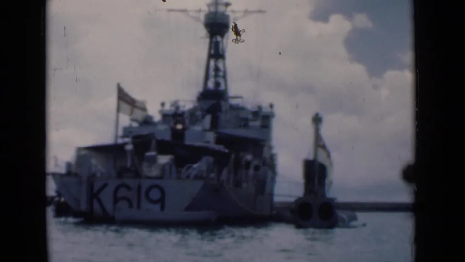 1946 Colombo harbor view of a naval vessel marked K619, framed from the stern with flags, rigging, water, and cloudy sky visible.