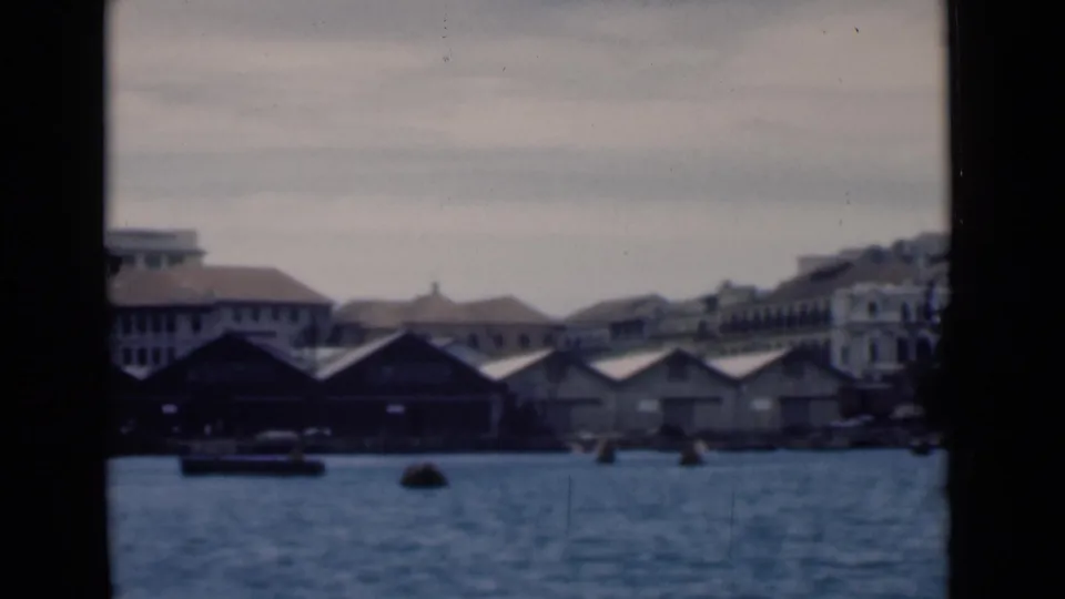 1946 Colombo waterfront with quay sheds, larger buildings, harbor water, and small boats seen from a vessel.