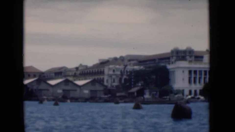 1946 Colombo port view with buoys in the foreground, quay sheds, and multistory waterfront buildings beyond.