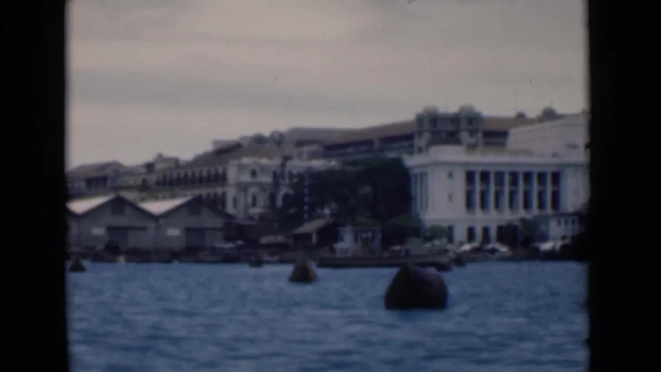 1946 Colombo harbor view from the water, showing a large white waterfront building, buoys, and small boats under a gray sky.