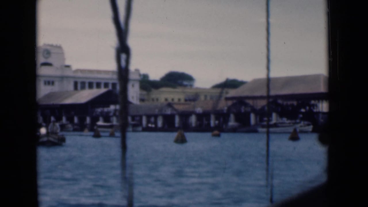 Covered docks, harbor water, buoys, and a clock-tower building seen through boat framing.