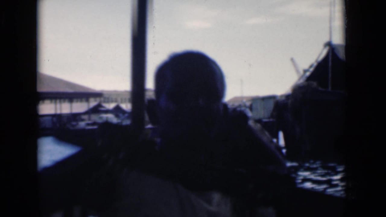 Two dark passenger silhouettes seen through a boat window with harbor structures beyond.