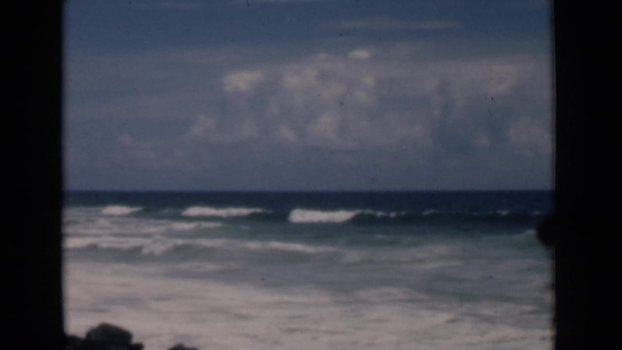 Ocean surf and a distant horizon under clouds, seen through dark film-frame edges.