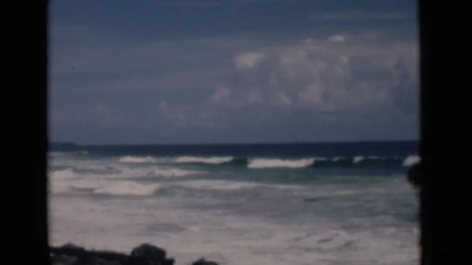 Soft 8mm frame of Colombo, Ceylon surf, with foamy nearshore water, a level horizon, clouds, and dark projected-frame borders.